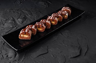 Lezzetli profiterollerin zarif sunumu. Çikolata soslu, parlak siyah tabakta.