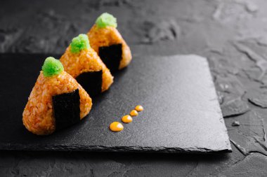 Canlı yeşil garnitürlü üç parça suşi siyah bir tahta yüzeyde ustalıkla sunuluyor.