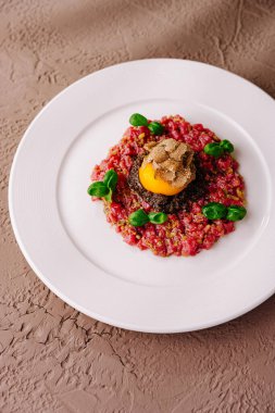 Üstü bıldırcın yumurtası ve siyah trüf mantarı ile kaplı, beyaz tabakta servis edilen zarif etli tart.
