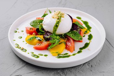 Burrata, domates ve beyaz tabakta taze fesleğen soslu caprese salatası.