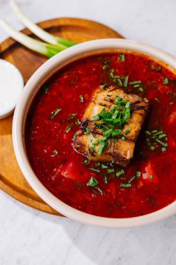 Bitkilerle süslenmiş canlı pancar çorbası ve kızarmış domuz eti, ekşi kremayla servis edilir.