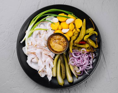 Sosis, domuz eti, turşu, soğan ve bir kase hardal içeren şarküteri tabağının üst görüntüsü.