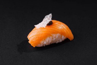 Nefis bir somon nigiri sushi 'nin yakın plan çekimi. Hassas bir malzemeyle süslenmiş, karanlık bir arka planda izole edilmiş.