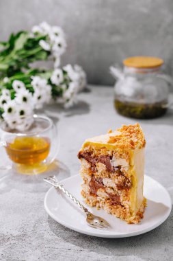 Beyaz bir tabakta servis edilen çok katmanlı ballı kekin yanında çay.