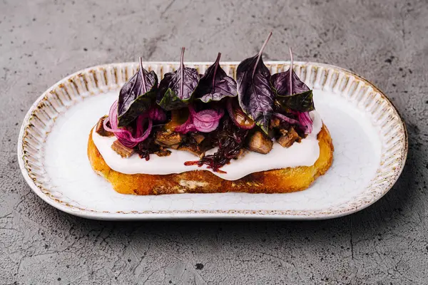 Krem peynirli, karamelli soğanlı ve seramik tabakta taze mor fesleğenli sanatsal tost.