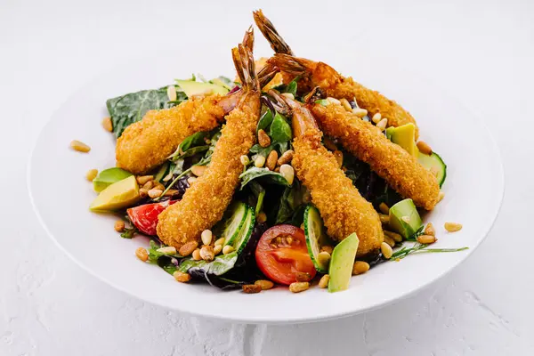 stock image Appetizing plate of breaded shrimp on a bed of greens with avocado, tomato, and pine nuts