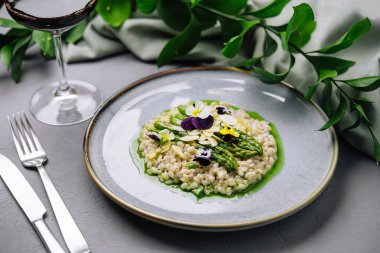 Kuşkonmaz uçlarıyla süslenmiş zarif bir tabak risotto ve renkli yenilebilir çiçekler, güzel bir yemek.