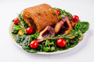 Beyaz arka planda ıspanak salatası, armut ve vişneli domatesle servis edilen leziz domuz rostosu.