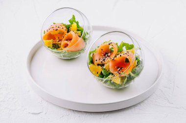 Şık cam kaselerde servis edilen sağlıklı füme somon salatası, karışık yeşiller ve susam tohumları.