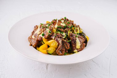 Taze sebze ve soslu ızgara biftek, beyaz tabakta servis edilir.