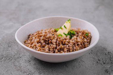 Mükemmel hazırlanmış karabuğday, bir tutam tereyağı ve taze bitkilerle süslenmiş seramik bir kasede.