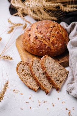Tahtada dilimlenmiş taze ekşi ekmek, beyaz bir masada buğday kulaklarıyla süslenmiş.