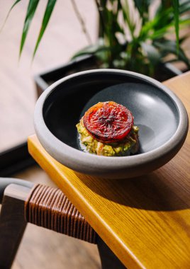 Siyah seramik tabakta ızgara domatesli, ahşap bir masada sunulan zarif avokado tostu.