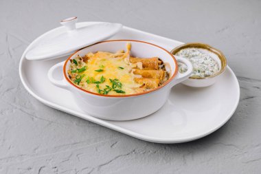 Erimiş peynirle fırında pişirilmiş lezzetli güveç ve taze otlar, beyaz bir tabakta servis edilir.