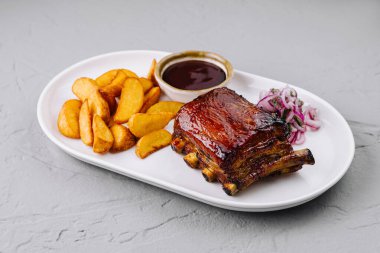 Beyaz tabakta patates dilimleri, bbq sosu ve lahana salatası ile nefis bir tabak domuz pirzolası.