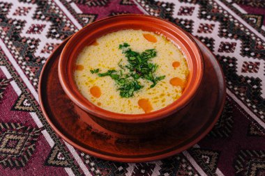 Canlı, kremalı, otlarla süslenmiş, terakotta kasesinde servis edilen bir çorbanın üst görüntüsü.