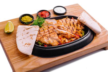 Baharatlı ızgara tavuk fajitası, tortilla ve ahşap bir tahtaya sosla servis edilir.