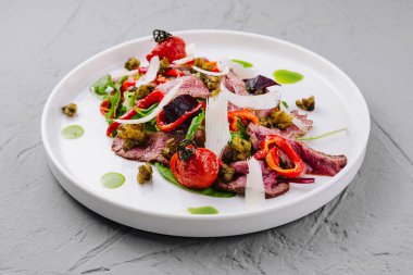 Modern bir tabakta servis edilen sebzeli, kaparili ve soslu biftek carpaccio.