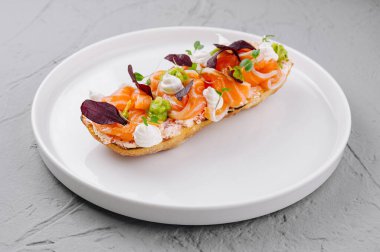 Zarif tütsülenmiş somon bruschetta otlar ve krem peynirle süslenmiş, temiz beyaz bir tabakta sunuluyor.