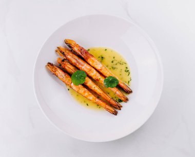 Beyaz tabak ve mermer zemin üzerinde kremalı sosla servis edilen lezzetli ızgara karides manzarası.