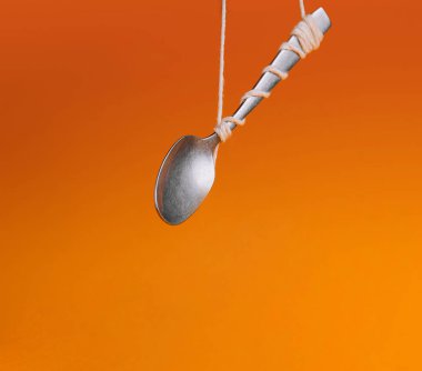 Silver spoon tied with string against a vibrant orange backdrop, creating an illusion of floating clipart