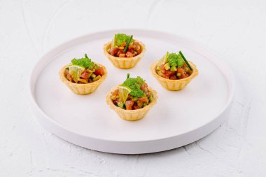 Dört renkli sebze turtası, yuvarlak beyaz bir tabakta otlarla süslenmiş.