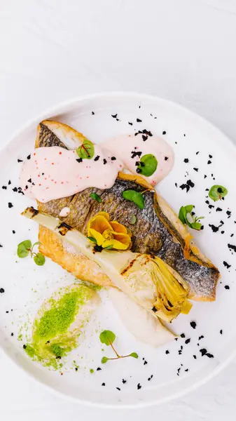Elegant presentation of a seared fish fillet with pink sauce, herbs, and edible flowers on a white plate