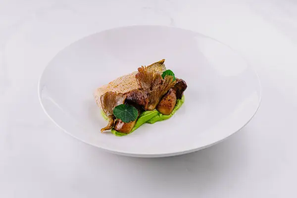 Elegant serving of seared fish over green pea puree with roasted mushrooms on a white plate