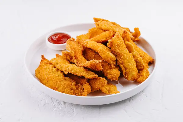 stock image Golden fried chicken tenders served on a white plate with ketchup, perfect for a quick snack or meal