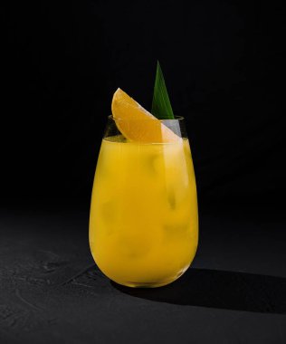 Koyu renkli bir taş yüzeyde, dilimlenmiş ve yaprakla süslenmiş turuncu bir kokteyl.