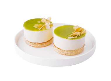 Beyaz bir tabakta badem dilimli iki ayrı limonlu cheesecake, beyaz arka planda izole edilmiş.