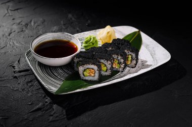 Siyah havyarla süslenmiş, soya sosu, wasabi ve zencefil ile servis edilen lüks suşi rulosu.