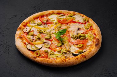 Koyu dokulu yüzeyde çeşitli malzemelerle canlı sebze pizzası.