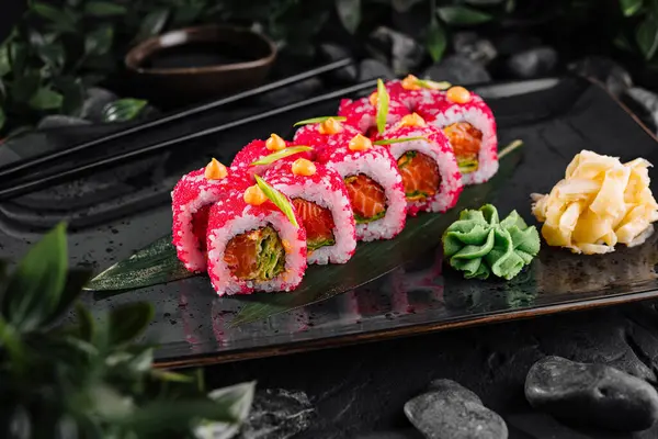 Exquisite sushi rolls adorned with fish roe on a sleek black plate, accompanied by wasabi and ginger