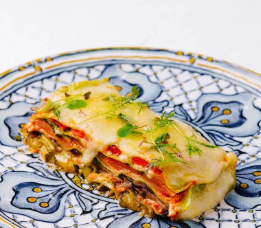 Bir dilim ev yapımı vejetaryen lazanya desenli bir tabakta otlarla süslenmiş.