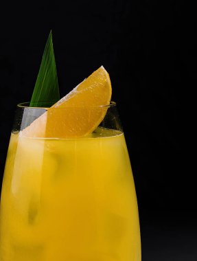 Koyu renkli bir taş yüzeyde, dilimlenmiş ve yaprakla süslenmiş turuncu bir kokteyl.