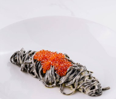 Beyaz tabakta kırmızı havyarla kaplanmış siyah mürekkep balığı makarnası.