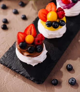 Üç mini pavlovas, çırpılmış krema ve taze böğürtlen servis tahtasında.