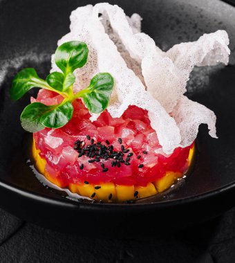 Susam tohumu ve bitkilerle kaplı, çıtır ekmekle servis edilen ton balıklı tartar sunumu.