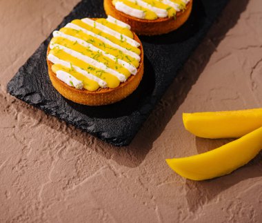 Üç lezzetli mango turtası kremalı ve limon aromalı, tahtada zarif bir şekilde servis ediliyor.