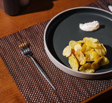 Modern yemek masasında bir tabak patatesli patates cipsi ve şık bir restoran atmosferine daldırılmış sos var.