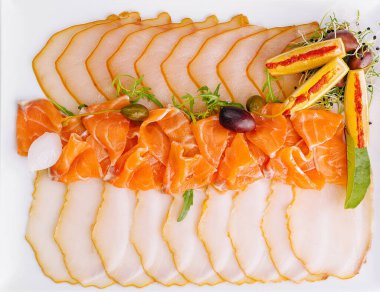 Tütsülenmiş somon ve bir tabakta beyaz balık dilimleri, otlar ve limonla süslenmiş.