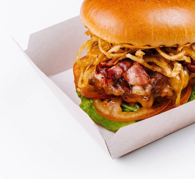 Açık bir karton kutuda, domuz pastırması ve malzemelerle birlikte iştah açıcı bir çizburger.