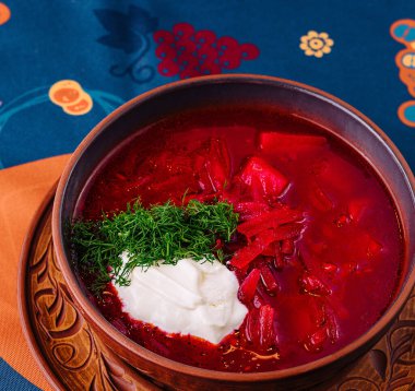 Ekşi krema ve dereotu desenli masa örtüsüyle süslenmiş canlı bir tas geleneksel borş.