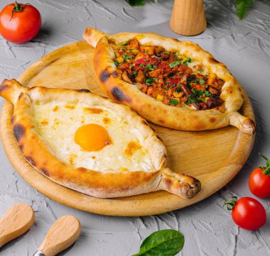Adjarian ve Imeretian Khachapuri, taze domateslerle servis edilir ve bitkilerle çevrilidir.
