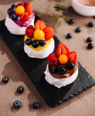 Üç mini pavlovas, çırpılmış krema ve taze böğürtlen servis tahtasında.