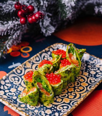 Somon ile doldurulmuş ve kırmızı havyarla kaplanmış zarif ıspanak krepleri dekoratif bir tabakta sunuluyor.