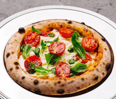 Lezzetli margherita pizza, domatesli ve fesleğenli, beyaz tabakta, siyah arka planda