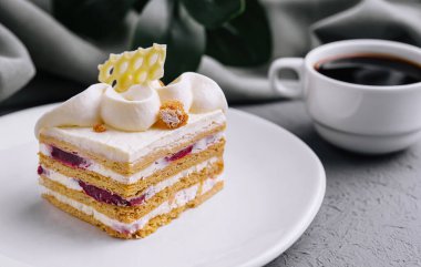 Katmanlı pastaya yakın çekim kremalı, kahveyle servis ediliyor.