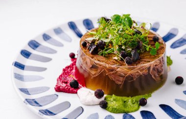 Beyaz arka planda çizgili bir tabakta servis edilen böğürtlenli ve mikro yeşillikli zarif jelatin aspic.